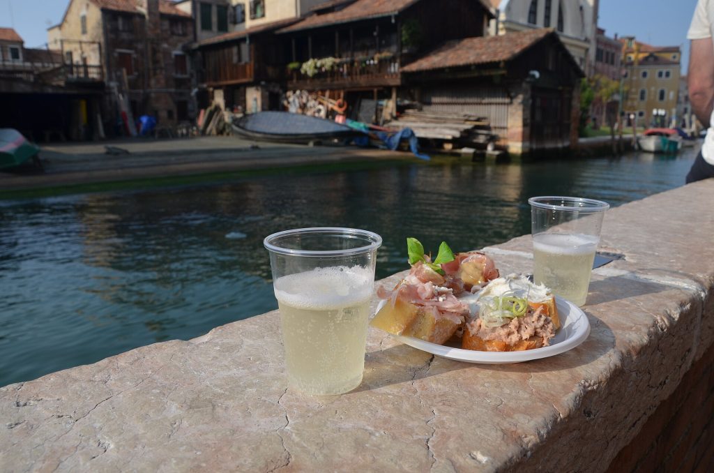 Cicchetti snacks and white wine beside a Venice canal